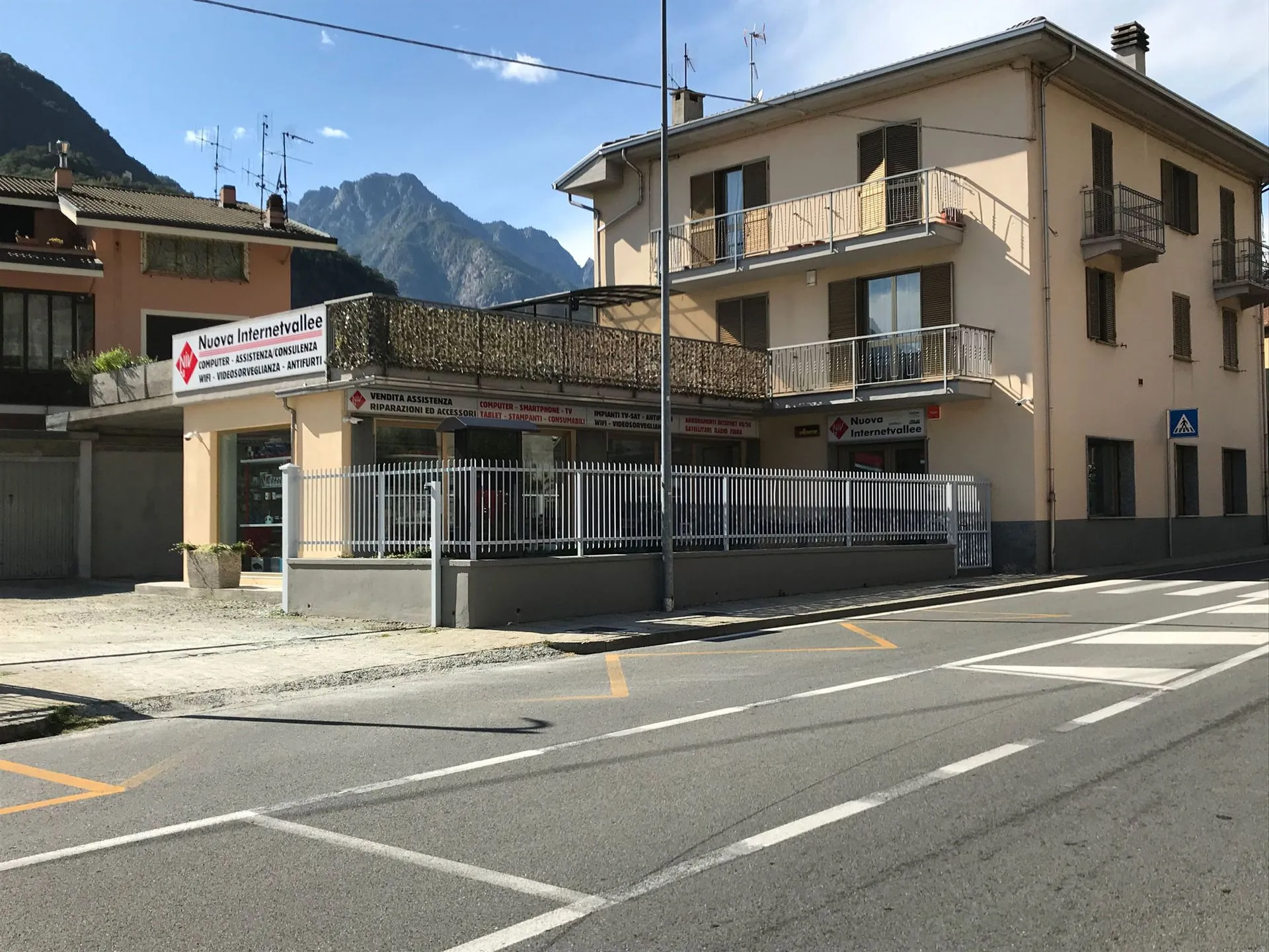 Negozio Nuova Internetvallee con insegne Computer Assistenza Consulenza, cancellata bianca e montagne alle spalle