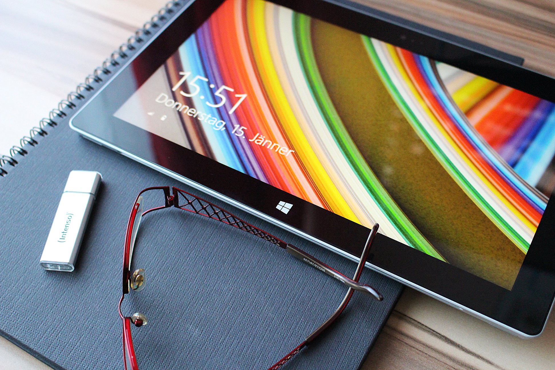 Tablet Windows con schermata di blocco alle 15:51, occhiali rossi e chiavetta USB Intenso su quaderno a spirale scuro
