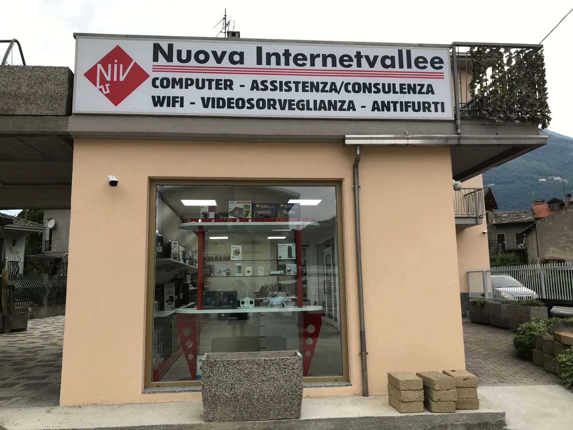 Negozio Nuova Internetvallee con insegna «Computer - Assistenza/Consulenza», vetrina con scaffali rossi e dispositivi